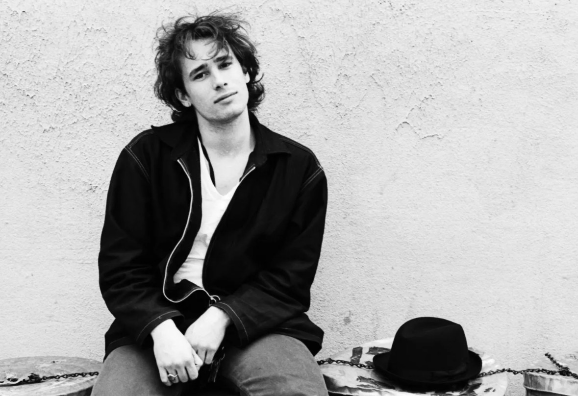Jeff Buckley sitting against a wall.